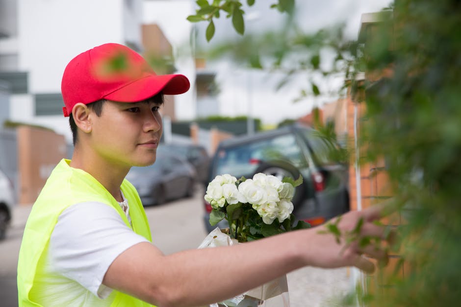 A young delivery person wearing a red cap and a high-visibility yellow vest is holding a bouquet of fresh white hydrangeas wrapped in white paper, preparing to deliver floral gifts. He is standing out